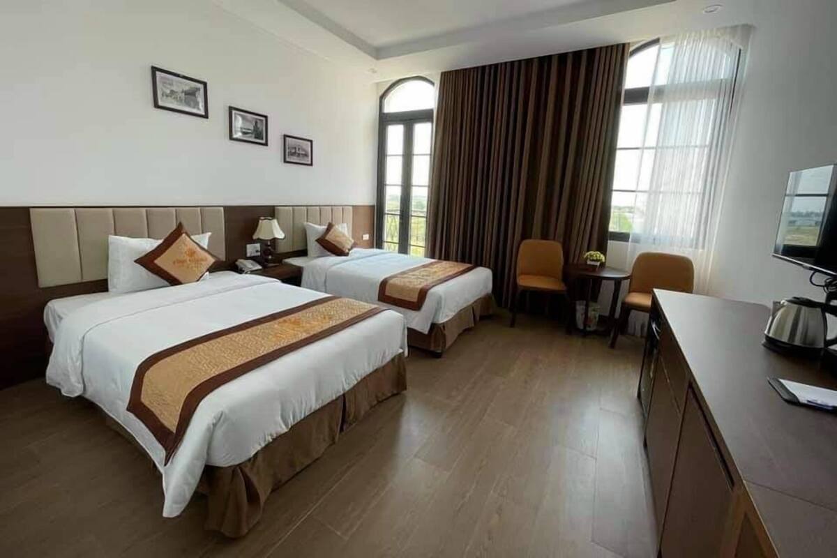 A hotel room with two beds, a desk, a chair, and a television.