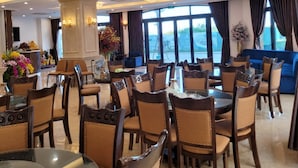 A spacious dining area with multiple tables and chairs, large windows with curtains, and a decorative pillar. - ViNH KHANG HA LONG HOTEL (Bai Chay)