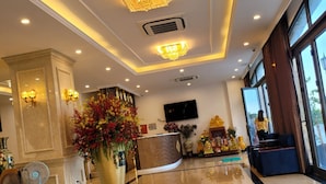 A hotel lobby with a reception desk, a large floral arrangement, and a seating area with a TV. - ViNH KHANG HA LONG HOTEL (Bai Chay)