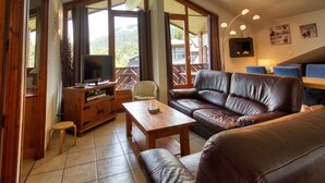 Una sala de estar con sofá, televisor, mueble de madera y un balcón con vistas al exterior.
