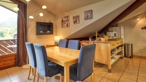 Un comedor con una mesa y sillas de madera, una lámpara, y una zona de cocina con microondas y refrigerador.