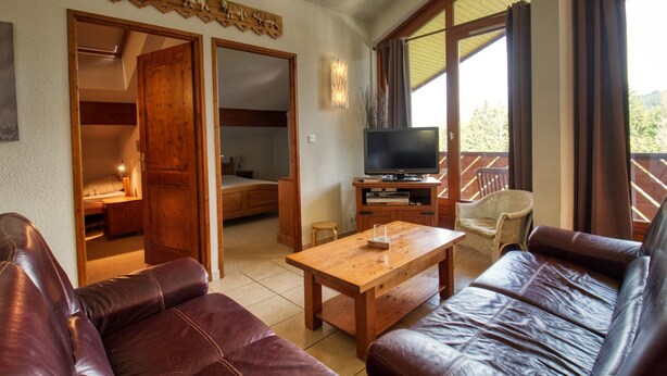 Una habitación con una mesa de centro de madera, sofás de cuero, televisión y un balcón con vistas.