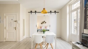 A dining area with a white table, two white chairs, a yellow pendant light, and a view of a cityscape through large windows. - Macflats Ayuntamiento (Valencia)