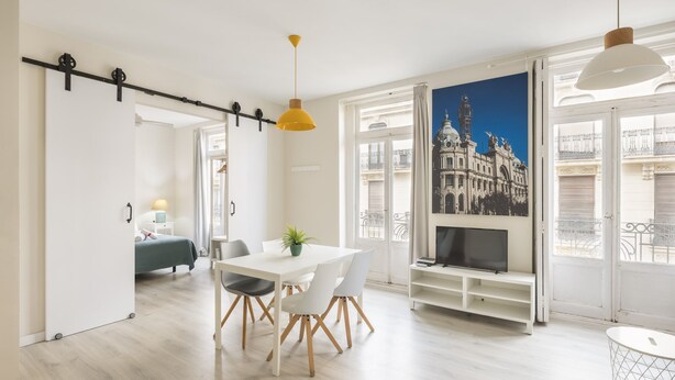 A modern living room with a dining area, a TV, and a large window with a cityscape view. - Macflats Ayuntamiento (Valencia)