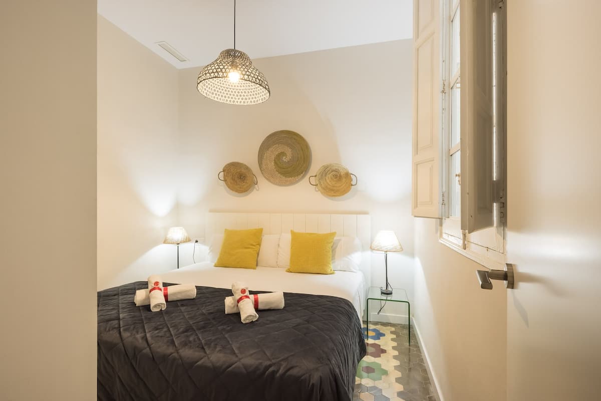 Hotellihuone, jossa on sänky, kaksi yöpöytävalaisinta, riippuvalaisin ja koristeelliset seinälevyt.
