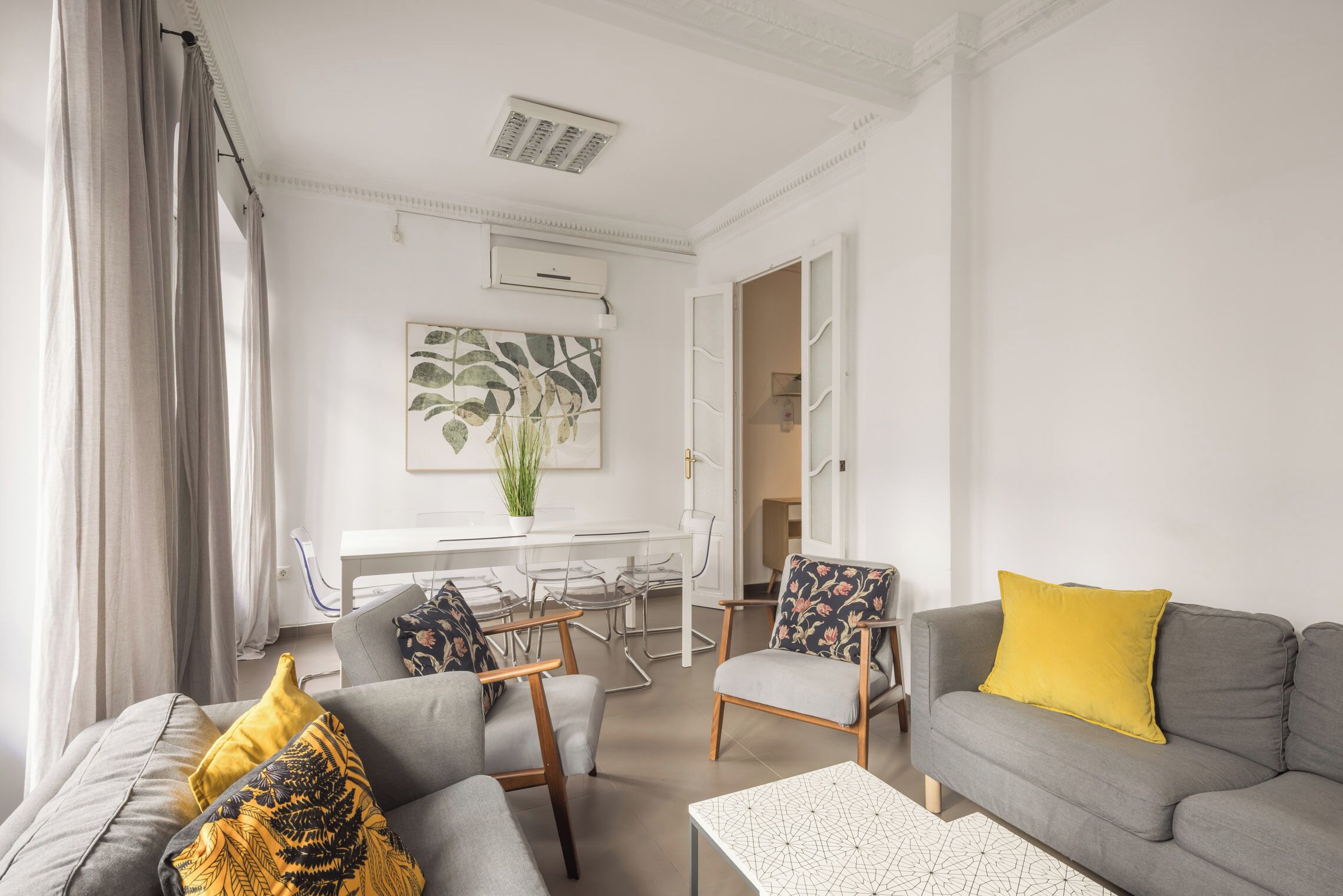 Een moderne woonkamer met een grijze bank, een salontafel en een eethoek met een witte tafel en stoelen.