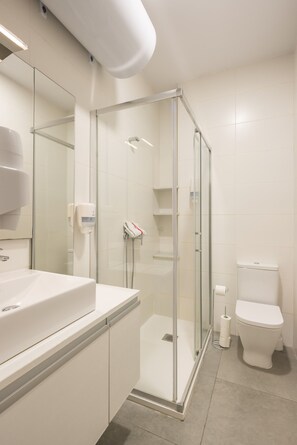 A modern bathroom with a glass shower enclosure, a white sink, and a toilet. - Macflats Ayuntamiento (Valencia)