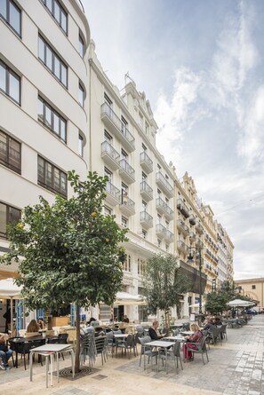 An outdoor cafe area with tables and chairs, surrounded by buildings with balconies and windows. - Macflats Ayuntamiento (Valencia)