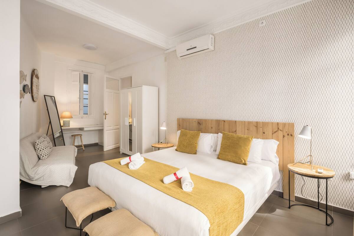 Hotellihuone, jossa on suuri sänky, yöpöydät, tuoli, penkki ja vaatekaappi.