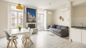 A modern living space with a dining area, a gray sofa, and a kitchen. - Macflats Ayuntamiento (Valencia)