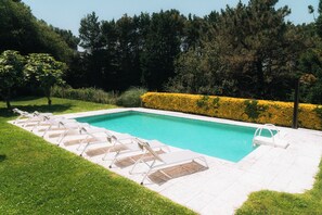 Une piscine rectangulaire dotée d’une terrasse carrelée et de chaises longues.