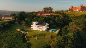 Une grande maison moderne dotée d’une piscine, entourée d’une végétation luxuriante et située dans un paysage vallonné.