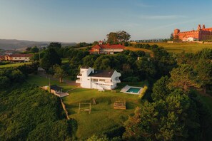 Una casa grande y moderna con piscina, rodeada de abundante vegetación y un paisaje montañoso.