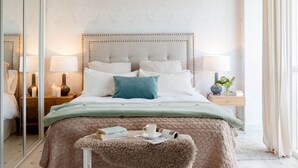 Une chambre à coucher avec un grand lit, des tables de chevet, un miroir et un luminaire suspendu.
