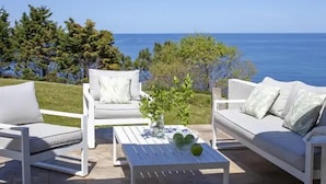 Une terrasse dotée de mobilier blanc, d’une table basse et offrant une vue sur l’océan.