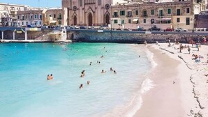 A coastal town with a prominent church, a sandy beach, and a clear blue sea. - 248 Boutique Studios (Sliema)