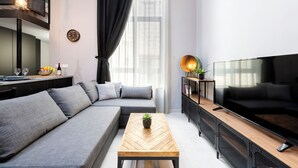 A modern living room with a sofa, a wooden coffee table, a TV, and a kitchen area with a dining table and chairs. - 248 Boutique Studios (Sliema)