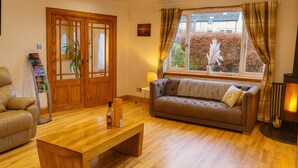 Een gezellige woonkamer met een houten vloer, een bruine bank, een houten salontafel en een open haard.