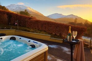 Un bain à remous avec vue sur les montagnes, une bouteille de champagne et un verre sur un plateau.