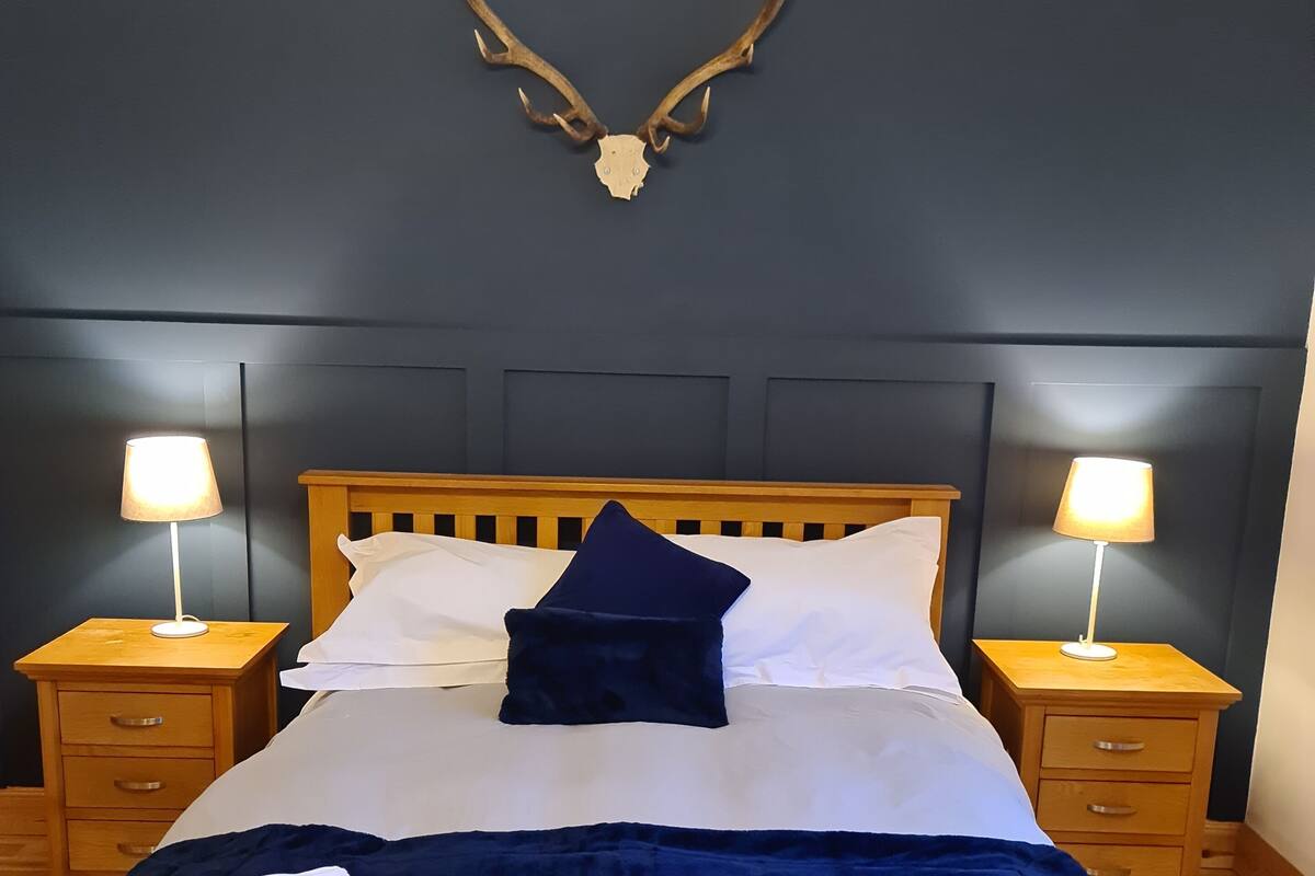 A bed with a dark blue bedspread, two white pillows, a dark blue pillow, and a folded white towel on the side.