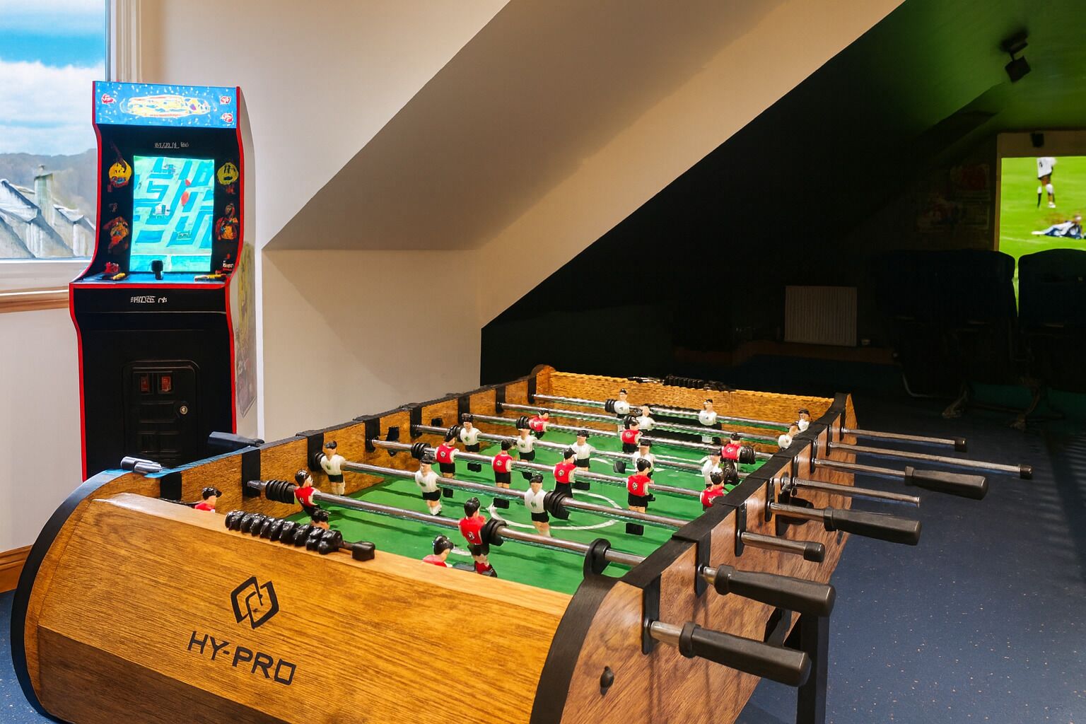 A foosball table with a wooden base and metal rods, a digital scoreboard, and a window with a view of mountains.
