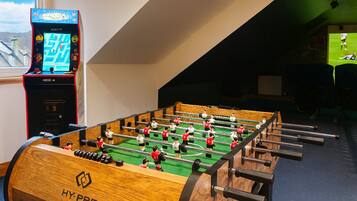 A foosball table with a wooden base and metal rods, a digital scoreboard, and a window with a view of mountains.