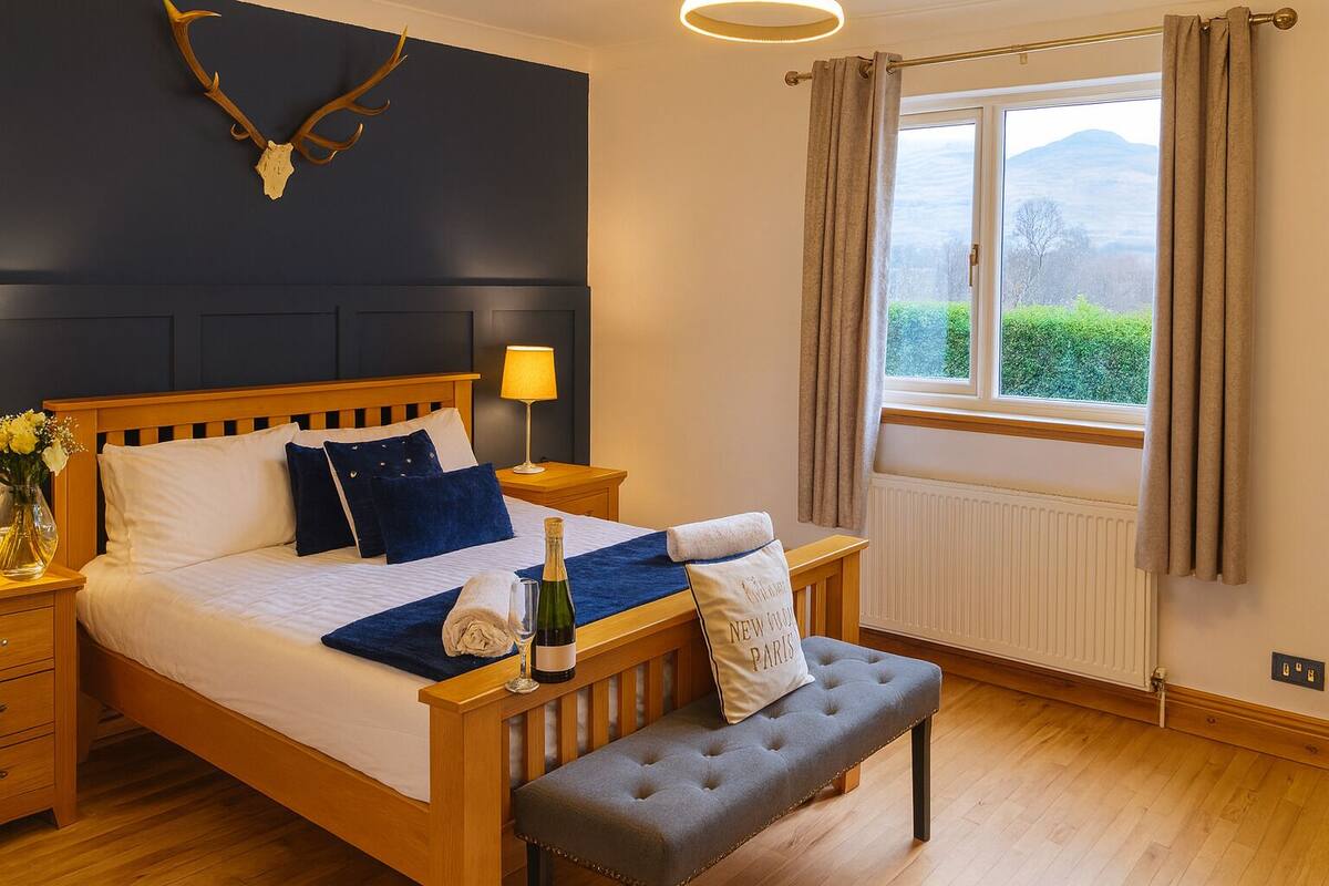 A neatly made bed with a bottle of champagne, a bedside lamp, and a bench.