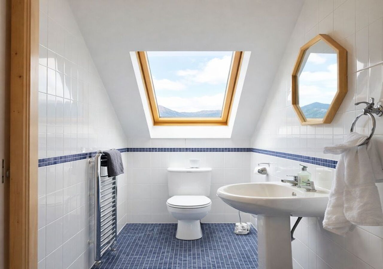 A small bathroom with a skylight, a toilet, a sink, and a mirror.