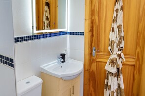 Une salle de bain avec un lavabo blanc, un miroir et une porte en bois sur laquelle est accrochée une serviette.
