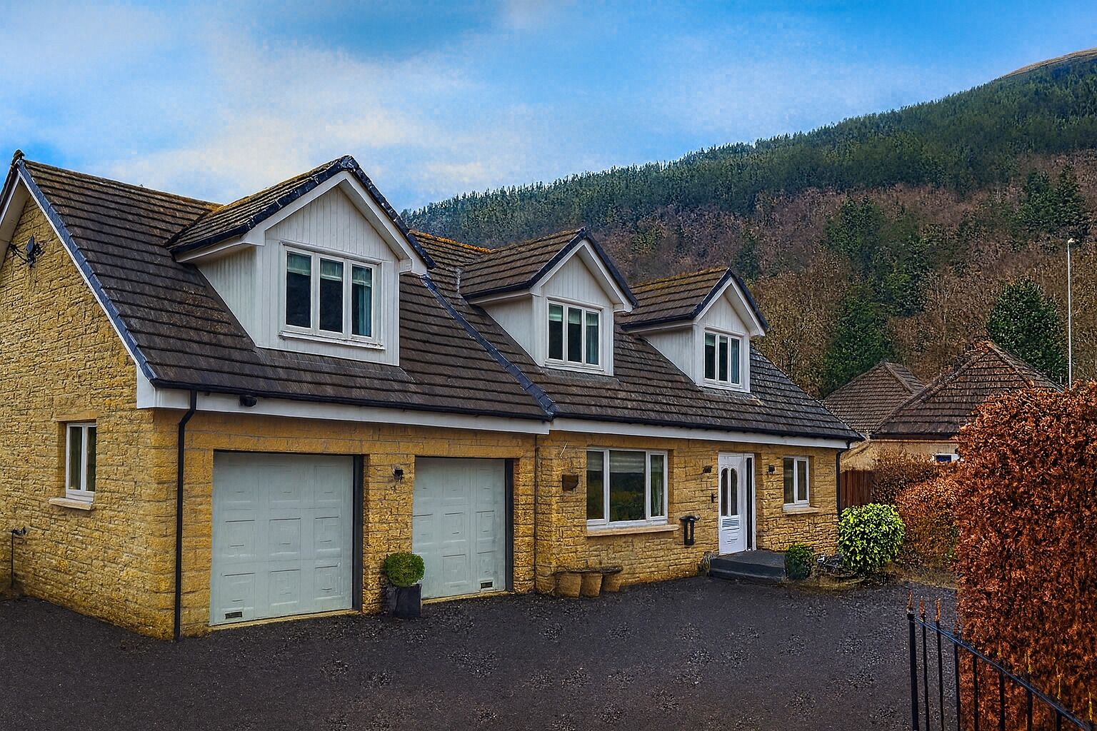 Ein zweistöckiges Haus mit Natursteinfassade, zwei Garagentoren und einem Hauseingang.