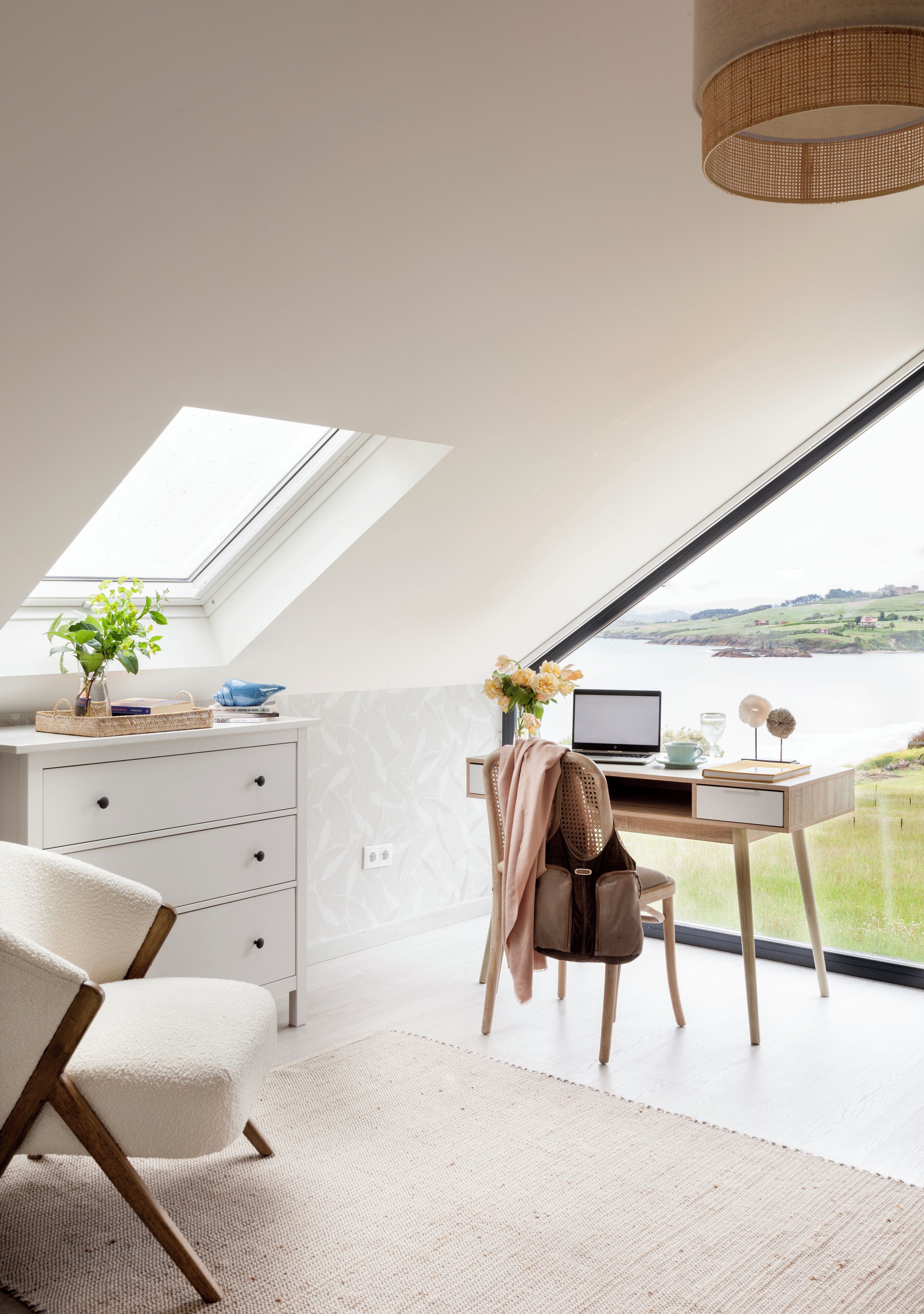 Une chambre moderne avec une lucarne, un bureau avec un ordinateur portable, une chaise et une vue sur un plan d’eau.