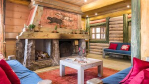 Interior acogedor de una cabaña de troncos con chimenea de piedra, mobiliario de madera y decoración rústica.