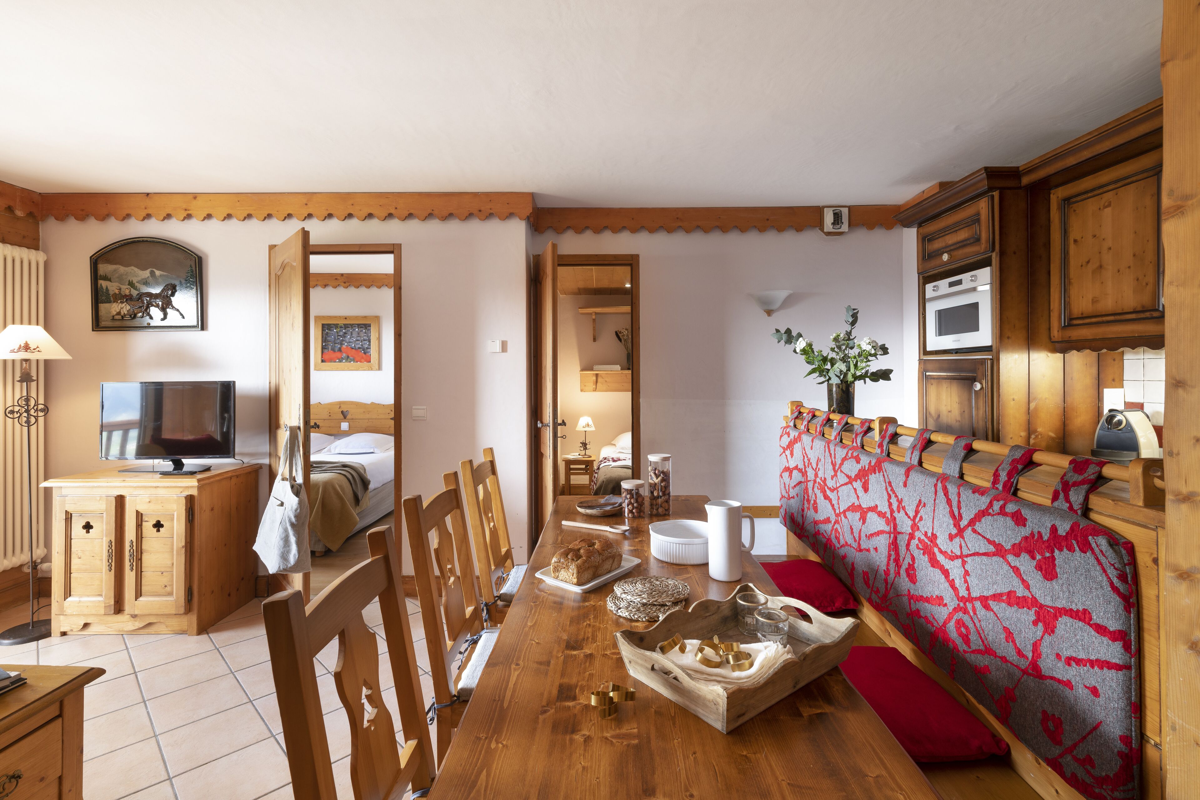 Une table à manger en bois avec des chaises, un téléviseur et un coin cuisine doté de meubles et d’appareils électroménagers en bois.