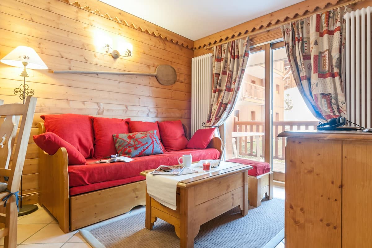 A cozy wooden cabin interior with a red sofa, a wooden coffee table, and a lamp.