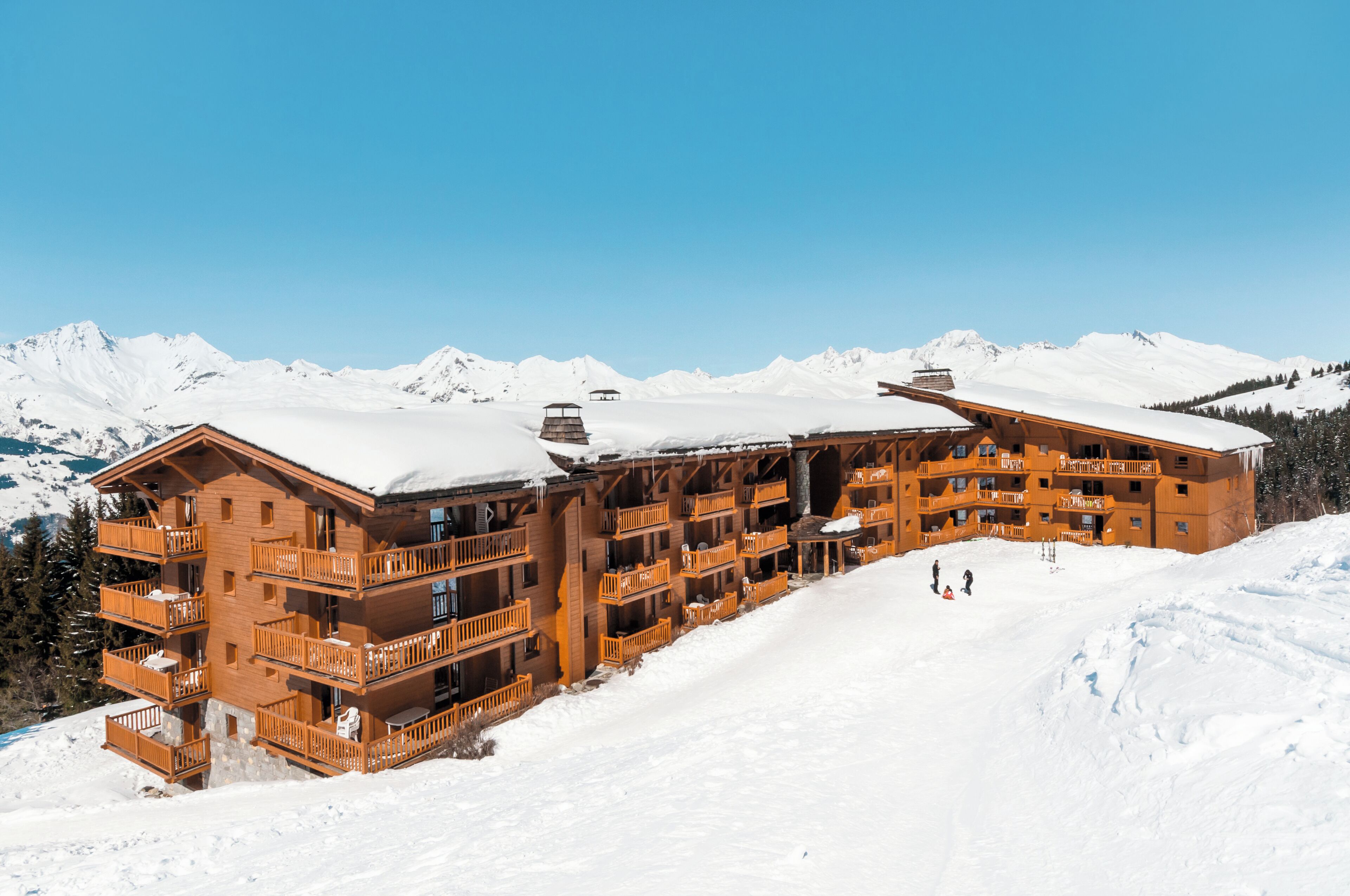 A large wooden lodge with multiple balconies and a ski slope in the background.