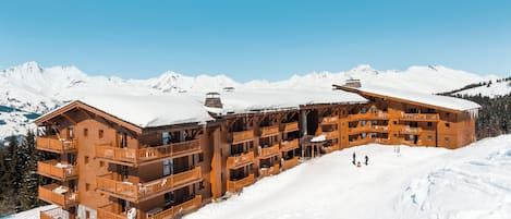 A large wooden lodge with multiple balconies and a ski slope in the background.