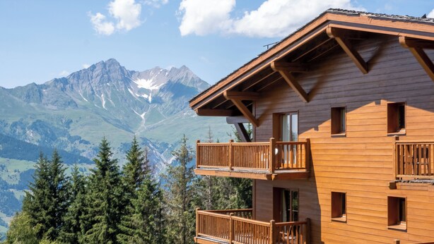 Un edificio de madera con balcones, vista a la montaña y cielo despejado.
