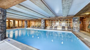 Una piscina interior con pilares de piedra, vigas de madera y sillones de descanso.