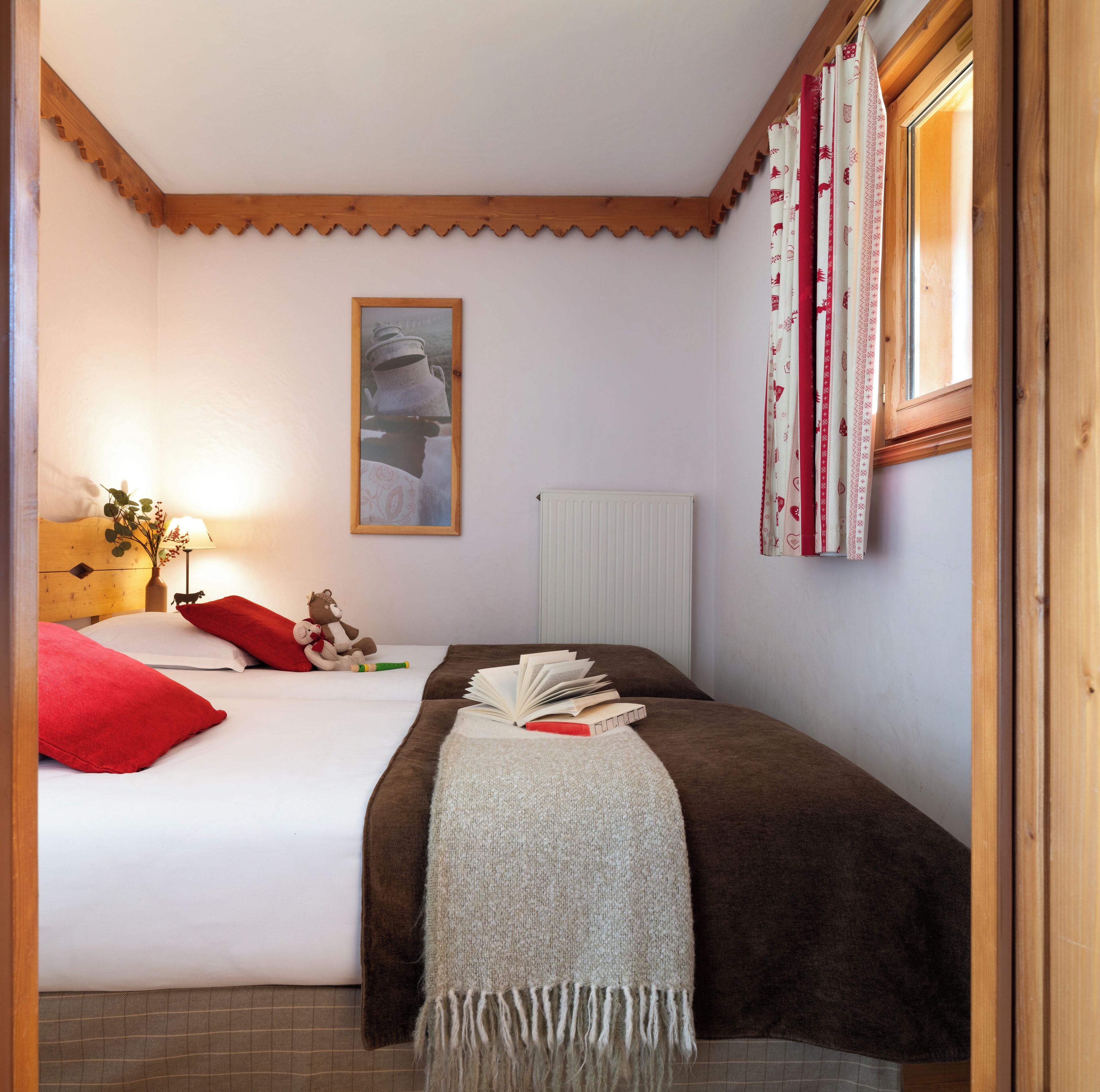 Une chambre à coucher avec un lit, une table de chevet avec une lampe, une fenêtre avec des rideaux et un tableau accroché au mur.