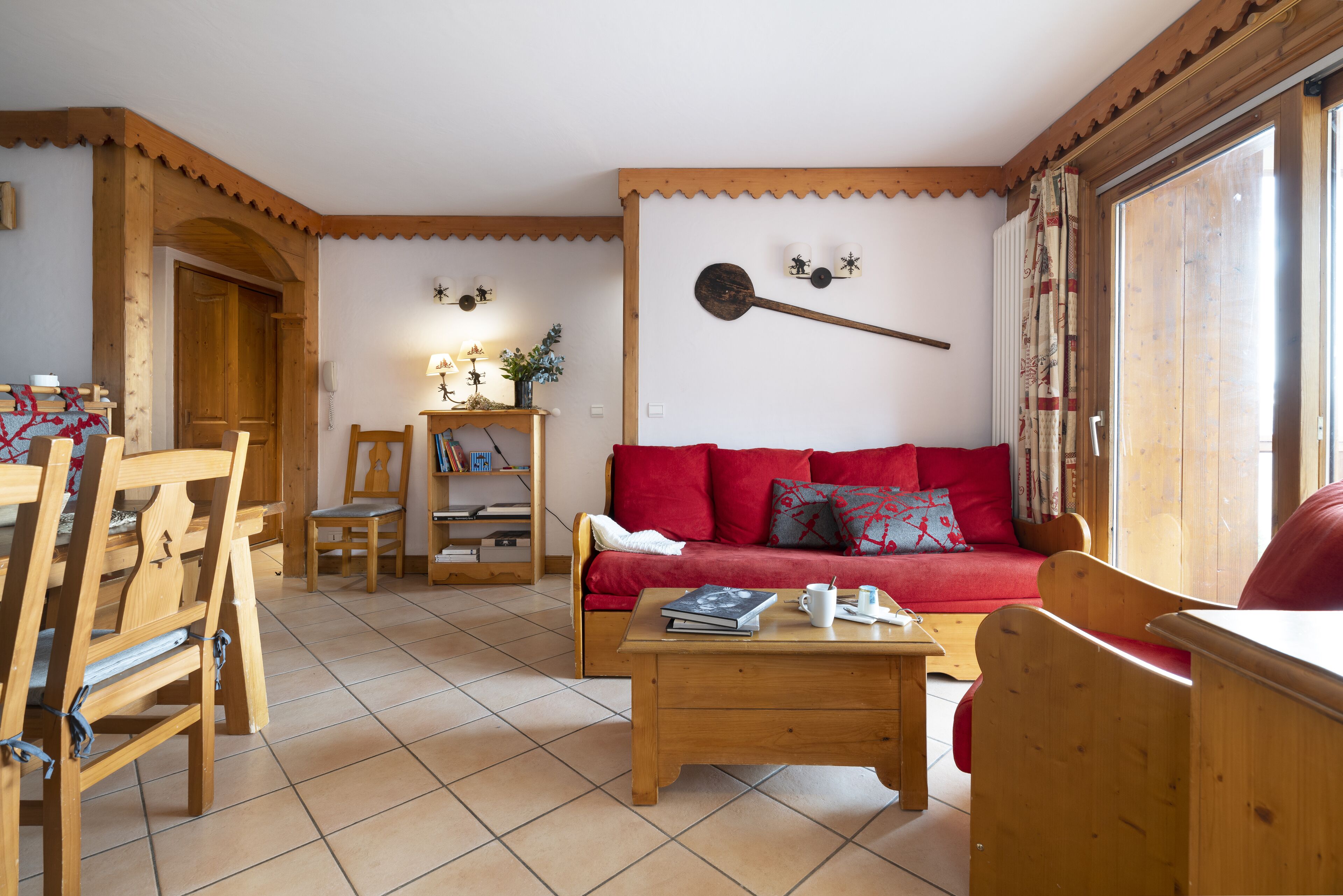 A cozy living room with a red sofa, wooden furniture, and a wooden ceiling.