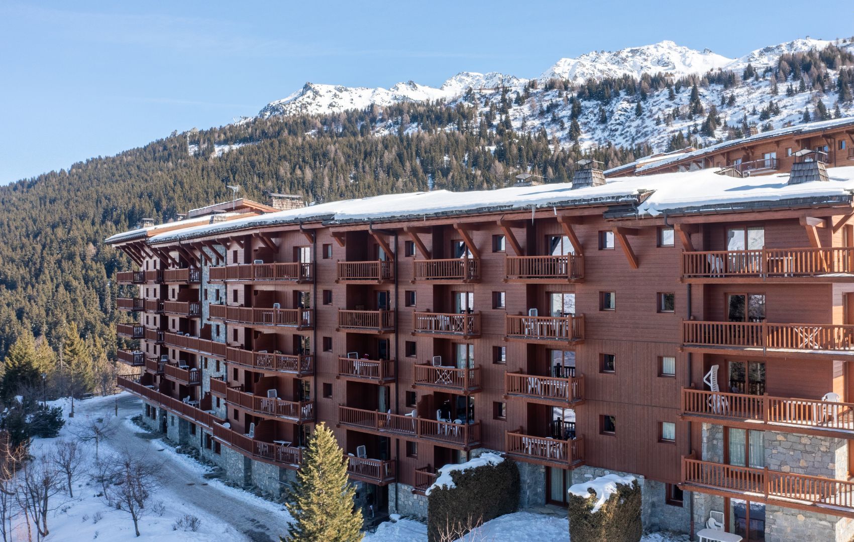 Un immeuble en bois à plusieurs étages, doté de balcons, entouré de montagnes enneigées.