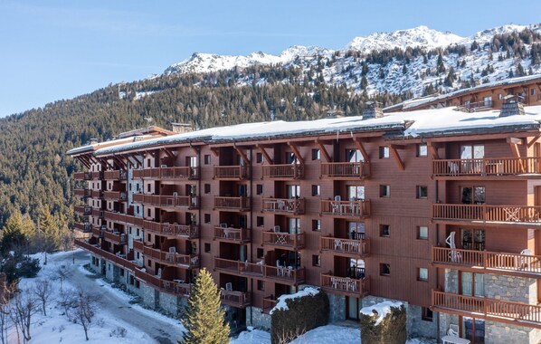 Un immeuble en bois à plusieurs étages, doté de balcons, entouré de montagnes enneigées.
