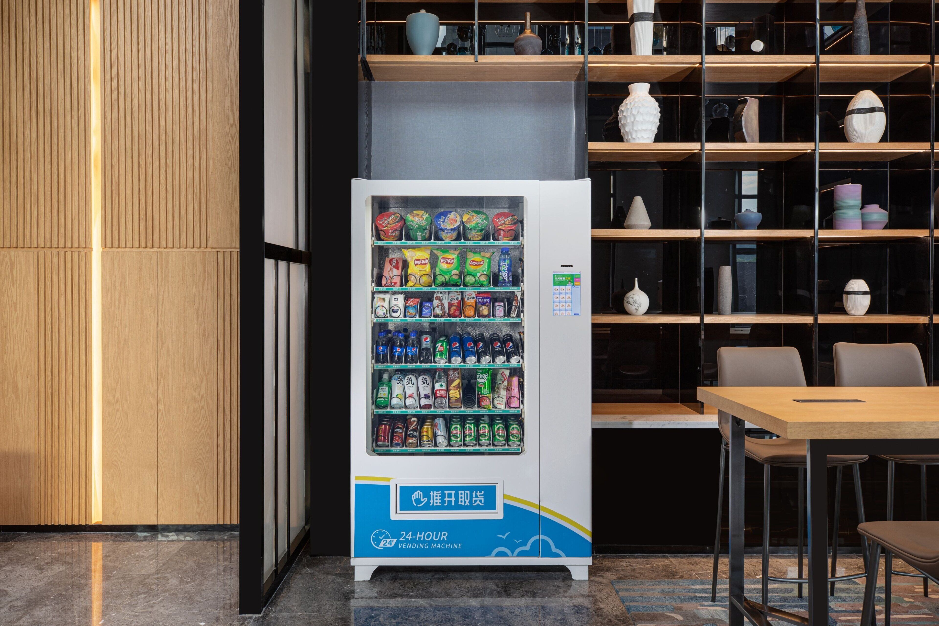 A vending machine with snacks and drinks, located in a modern interior with wooden paneling and shelves with decorative items.