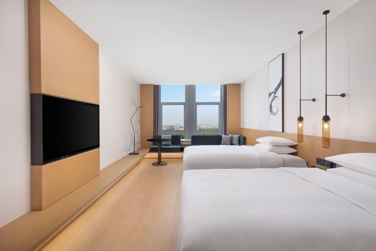 Ein modernes Hotelzimmer mit einem großen Bett, einem Flachbildfernseher, einer Sitzecke mit Blick und einem großen Fenster.