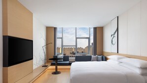 A modern hotel room with a large bed, a flat-screen TV, a seating area with a view of the city, and large windows. - Fairfield by Marriott Liaocheng Dongchangfu (Liaocheng)