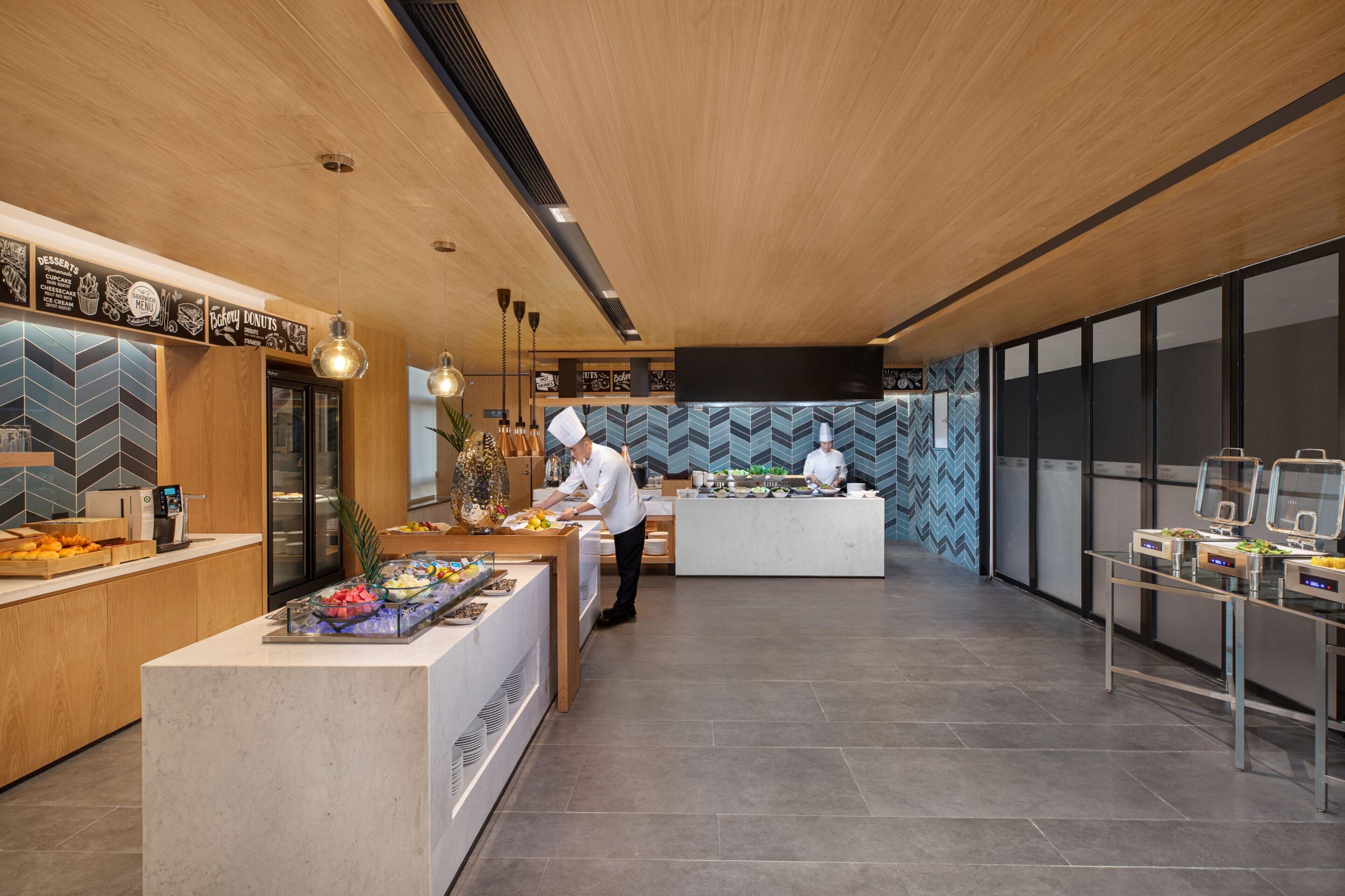 Una cocina moderna con detalles de madera, una zona de bufé con diversas opciones de comida y un piso de baldosas limpias.