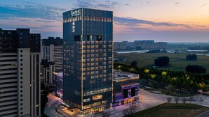 A high-rise hotel with a modern glass facade, surrounded by other buildings and a park. - Fairfield by Marriott Liaocheng Dongchangfu (Liaocheng)