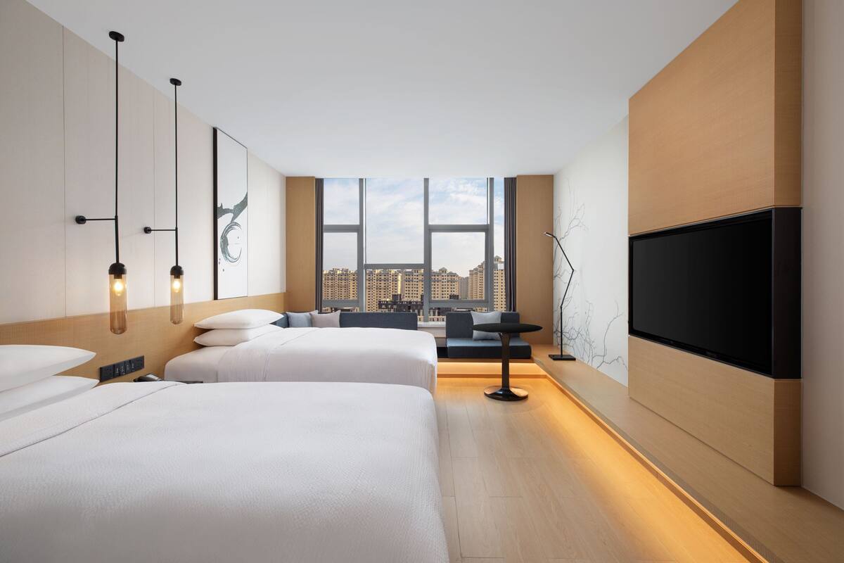 Ein modernes Hotelzimmer mit zwei Betten, einem Fernseher und Blick auf die Stadt.