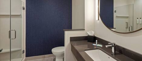 A modern bathroom with a glass shower enclosure, a white toilet, and a dark blue textured wall.