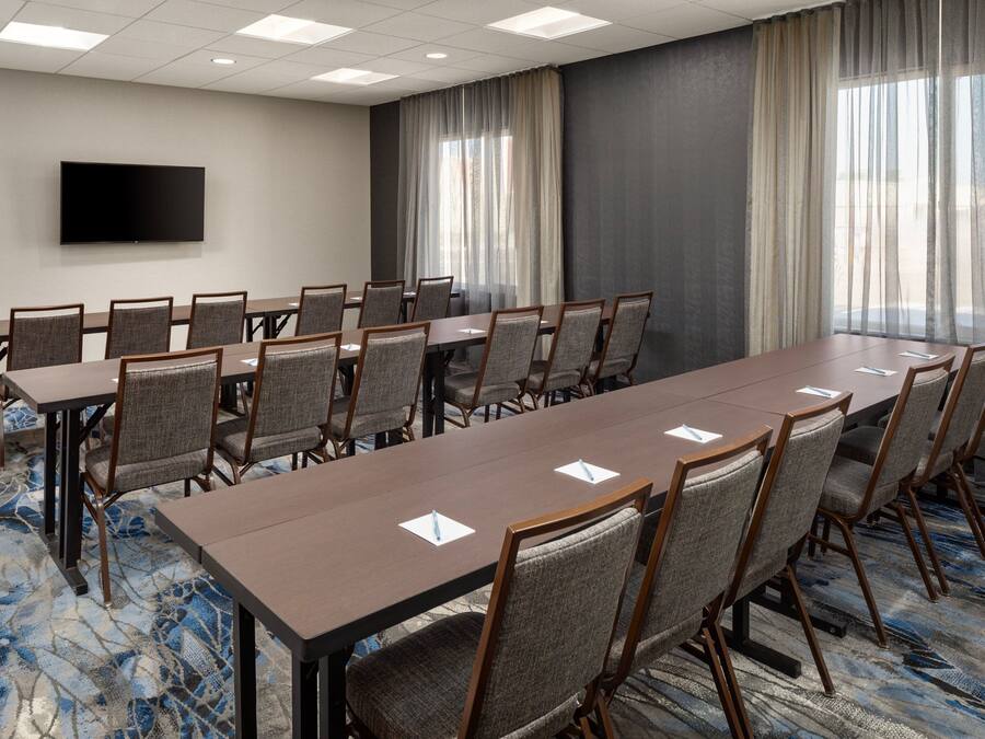 A conference room with a long table, chairs, a flat-screen TV, and large windows with curtains.